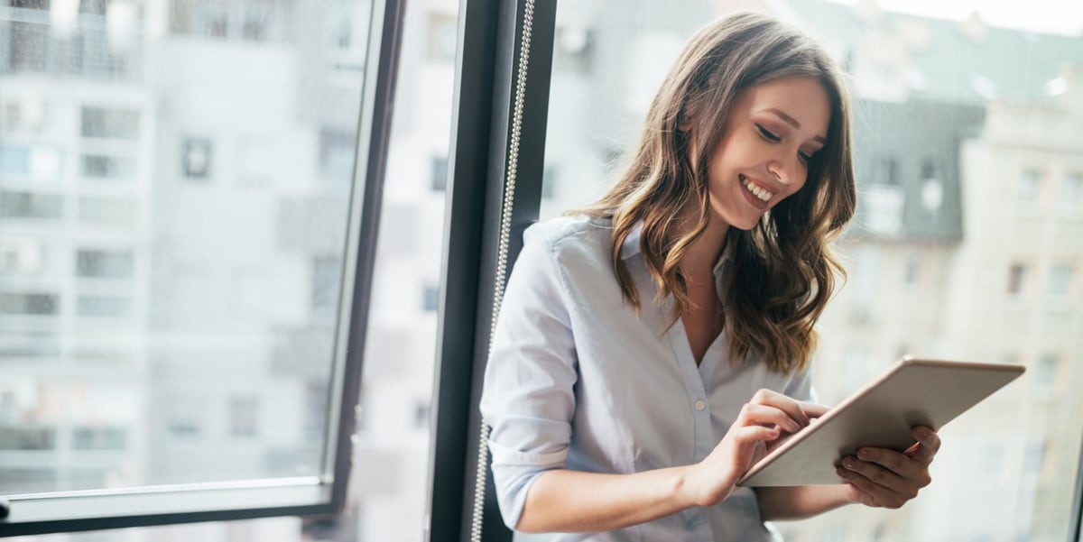 woman in office, sitting by window, looking at tablet