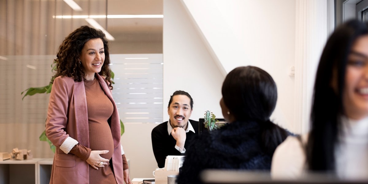 woman in office speaking to colleagues seated at a table